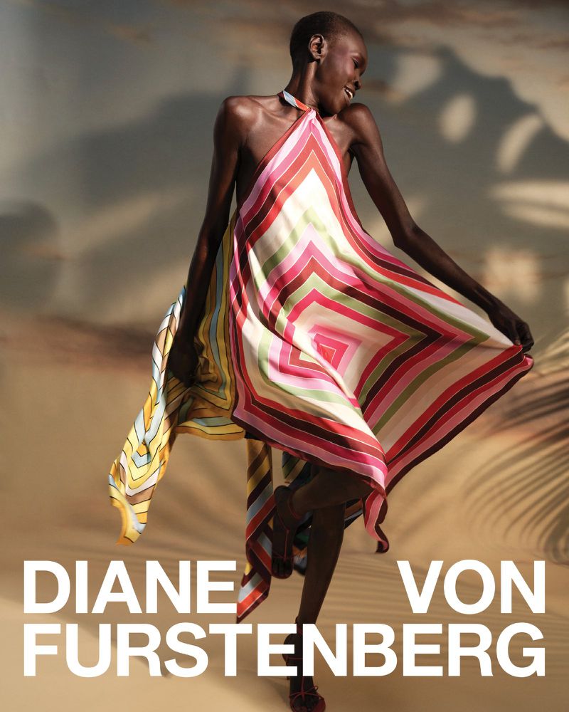 Elegant shot of a Black female model wearing a colorful Diane von Furstenberg dress, standing against a tan background with palm tree shadows.