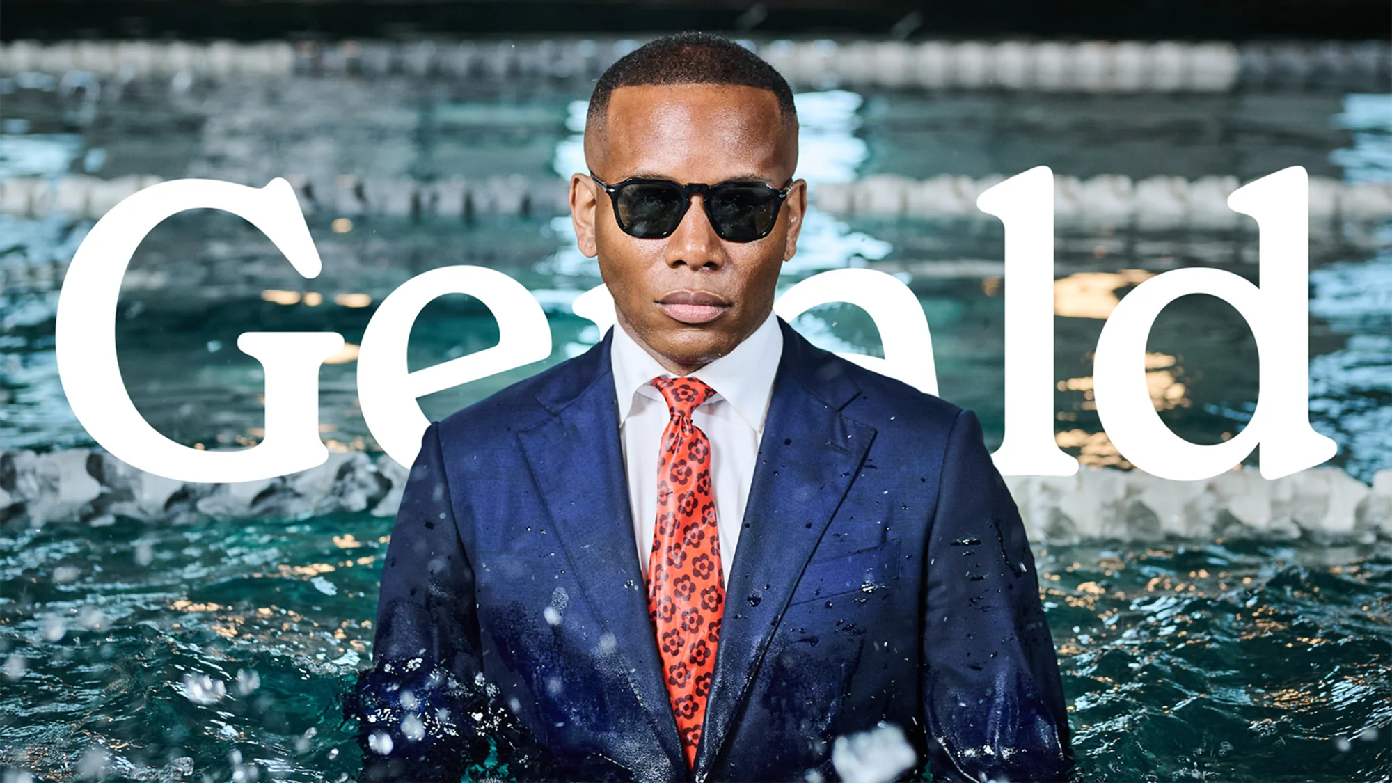 Man in suit stands in pool with sunglasses. The shot is medium framing of water and body with text overlayed 'Gerald'.