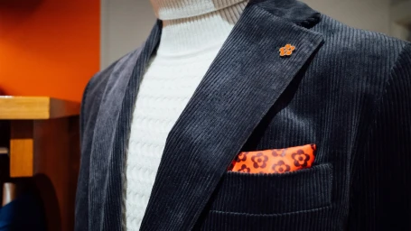 Close-up of a man wearing a dark corduroy blazer over a white turtleneck sweater with a patterned pocket square.