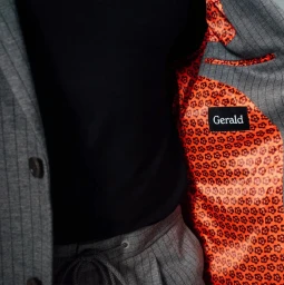 Close-up of a person wearing a grey pinstripe suit jacket and trousers with a black shirt and bright orange floral lining