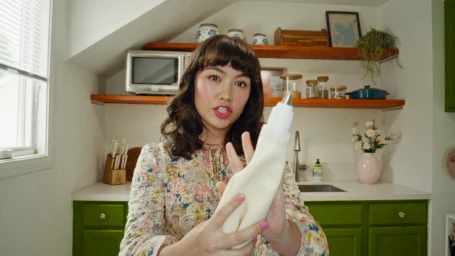 A woman in a floral blouse holding a squeeze bottle in a green and white kitchen for Idahoan Get Real campaign.