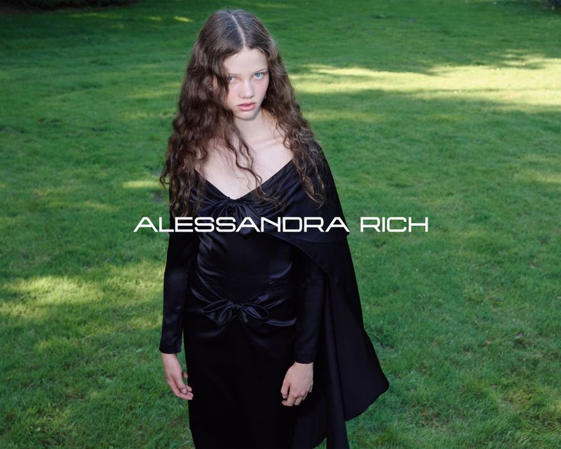 Young woman poses in black dress outdoors on a grassy lawn. The fashion shot includes visible text that reads: ALESSANDRA RICH.
