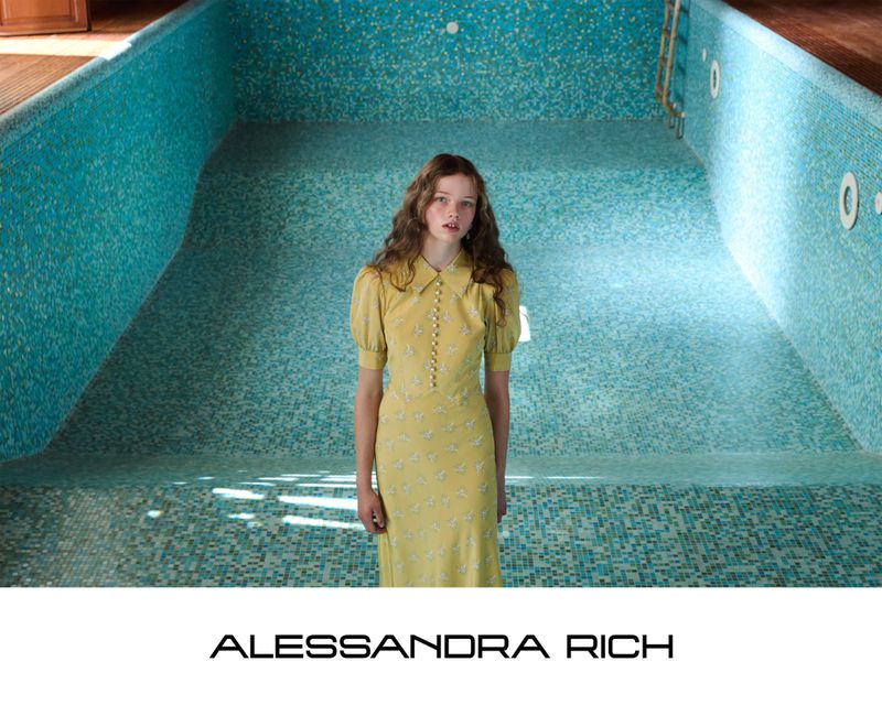 Young woman in a yellow dress stands inside an empty swimming pool with light blue tiles, creating a unique and visually striking composition.
