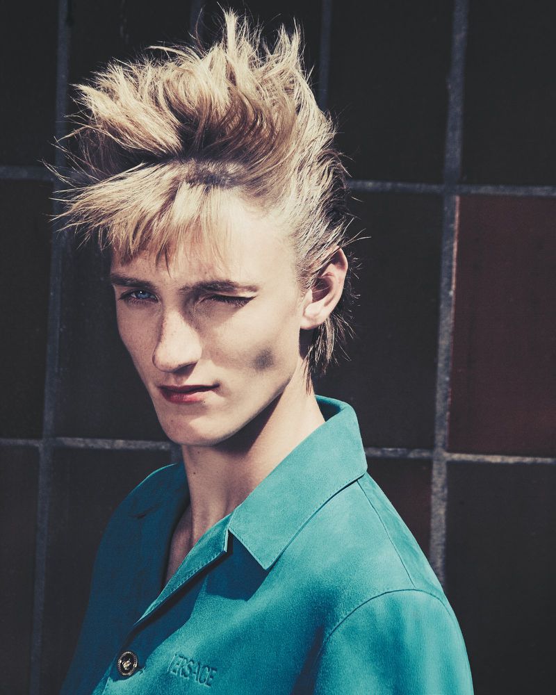 Close-up portrait of an adult male fashion model with a turquoise button-down shirt with blonde hair, winking one eye.