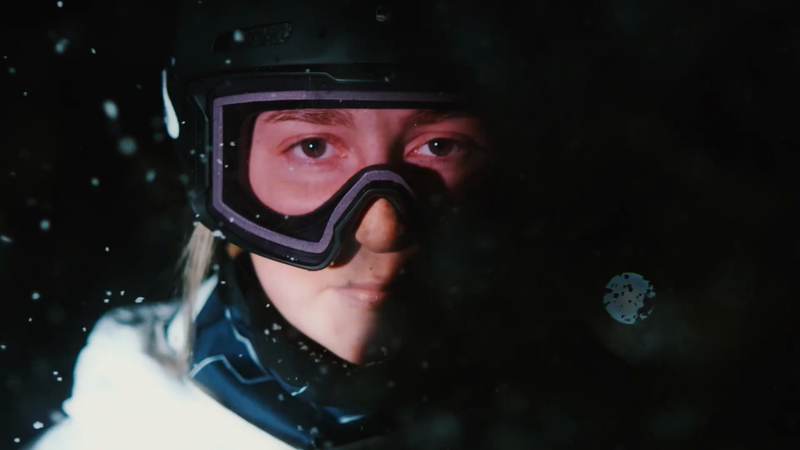 Close up of a person wearing a ski helmet and goggles in a dark snowy environment. Focus on eyes and goggles.