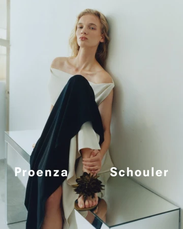 Fashion editorial shot of a woman wearing an off-the-shoulder top and black skirt sitting on a reflective table indoors.