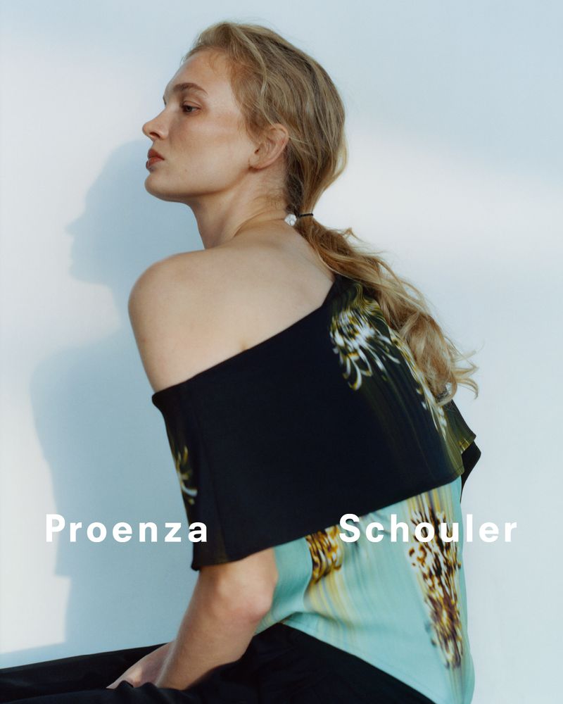 Blonde woman in off-the-shoulder Proenza Schouler top against a clean white background in a fashion editorial style photograph.