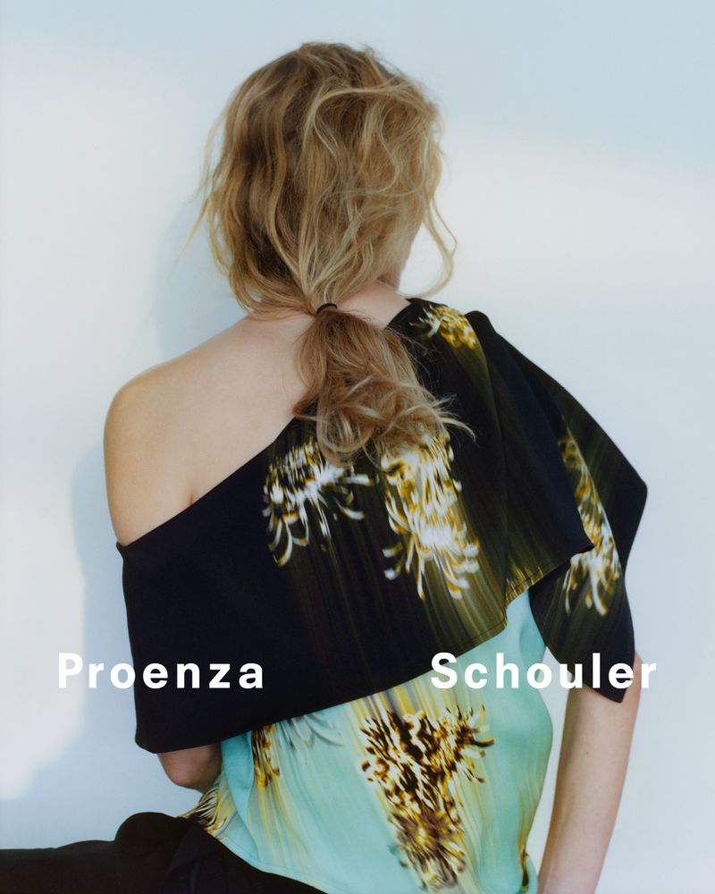 Woman with blonde hair in ponytail poses wearing Proenza Schouler fashion top in a studio. Shoulder and back are visible.