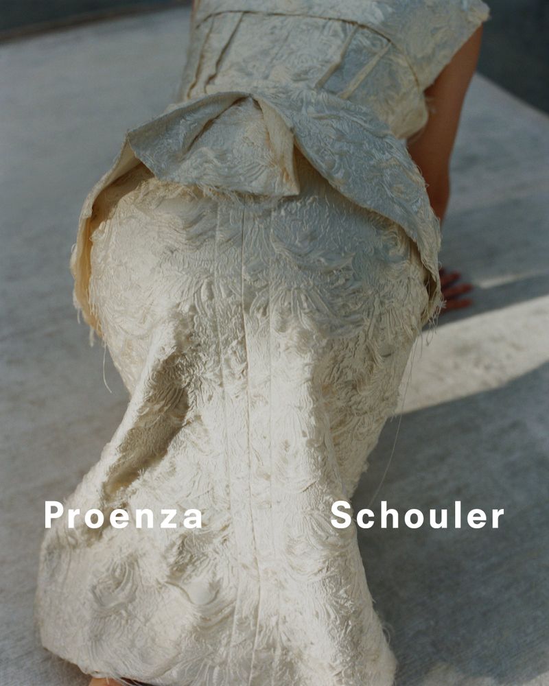 Close-up of a person wearing a textured, cream-colored Proenza Schouler dress with ruffles, posing on a concrete surface in natural light.
