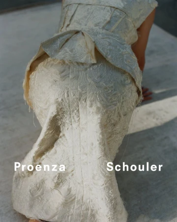 Close-up of a person wearing a textured, cream-colored Proenza Schouler dress with ruffles, posing on a concrete surface in natural light.