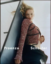 Model in textured red cardigan leaning against a dark architectural frame for Proenza Schouler