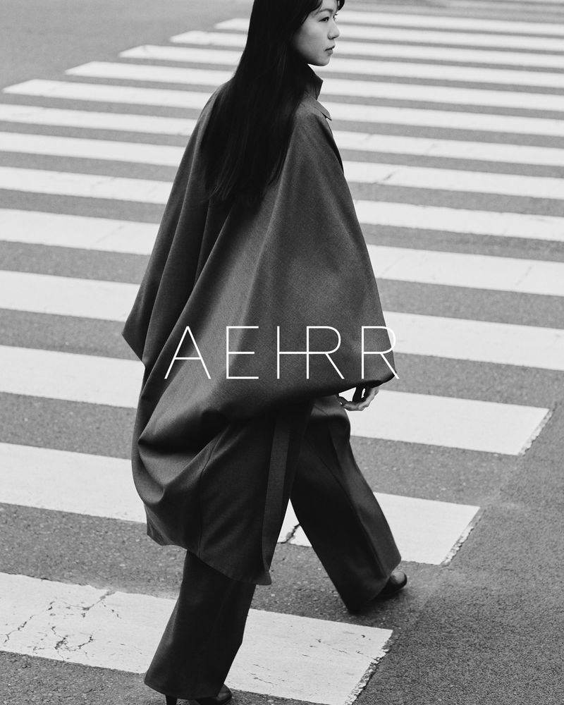 Woman in stylish poncho and trousers crossing a zebra street crossing, captured in black and white with a unique, eye-catching aesthetic.