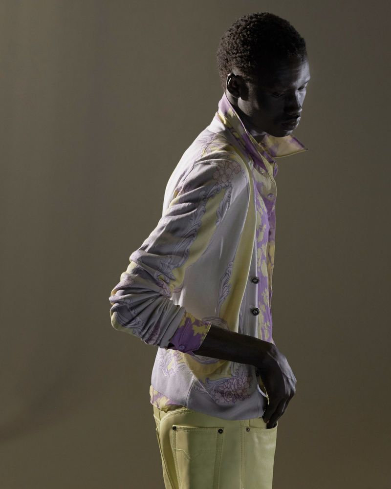 Fashion shot of a Black male model in a paisley jacket and yellow pants, posing in a studio with soft, directional lighting.