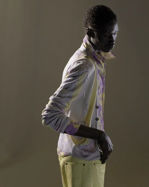 Fashion shot of a Black male model in a paisley jacket and yellow pants, posing in a studio with soft, directional lighting.