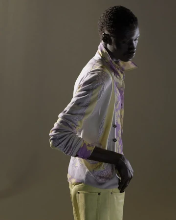 Fashion shot of a Black male model in a paisley jacket and yellow pants, posing in a studio with soft, directional lighting.