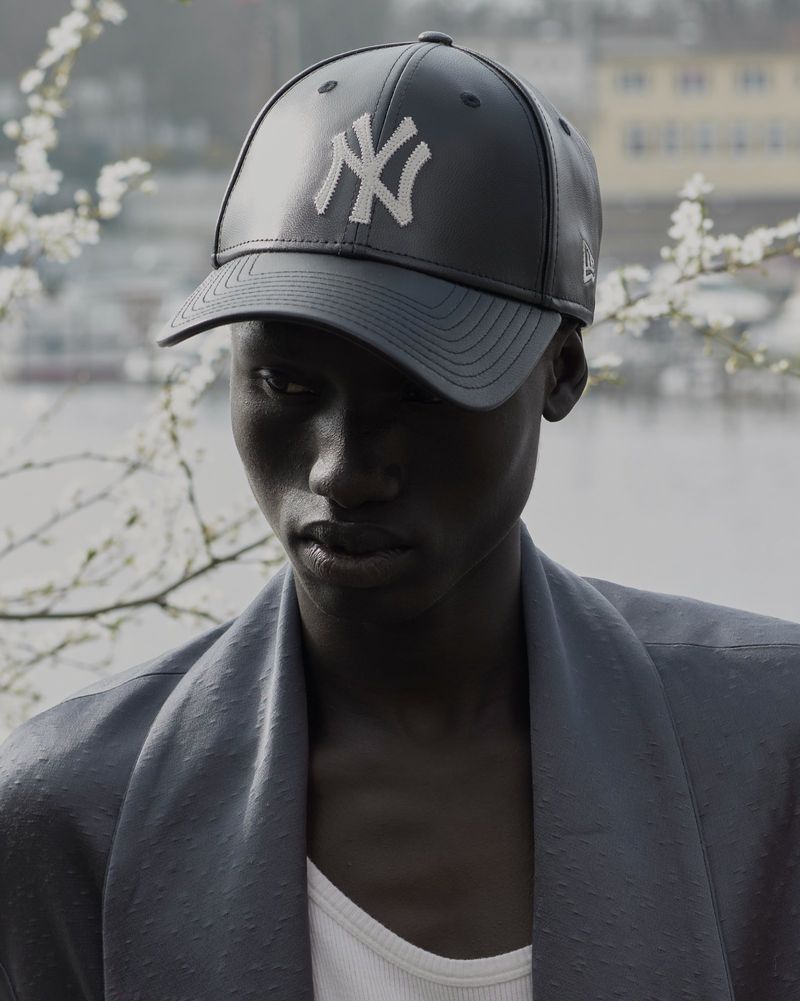Portrait of an adult wearing a New York Yankees baseball cap with blurred background, and wearing a jacket and tank top.