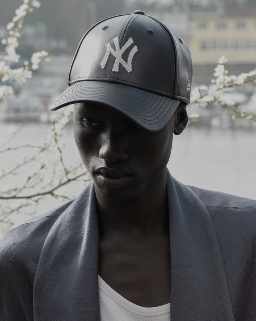 Portrait of an adult wearing a New York Yankees baseball cap with blurred background, and wearing a jacket and tank top.