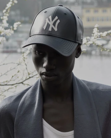 Portrait of an adult wearing a New York Yankees baseball cap with blurred background, and wearing a jacket and tank top.