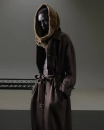 Model wearing a brown belted coat and hooded cowl against a neutral studio backdrop in Sapere Aude editorial.