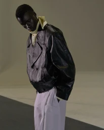 Model in a black leather jacket and white trousers against a neutral studio backdrop