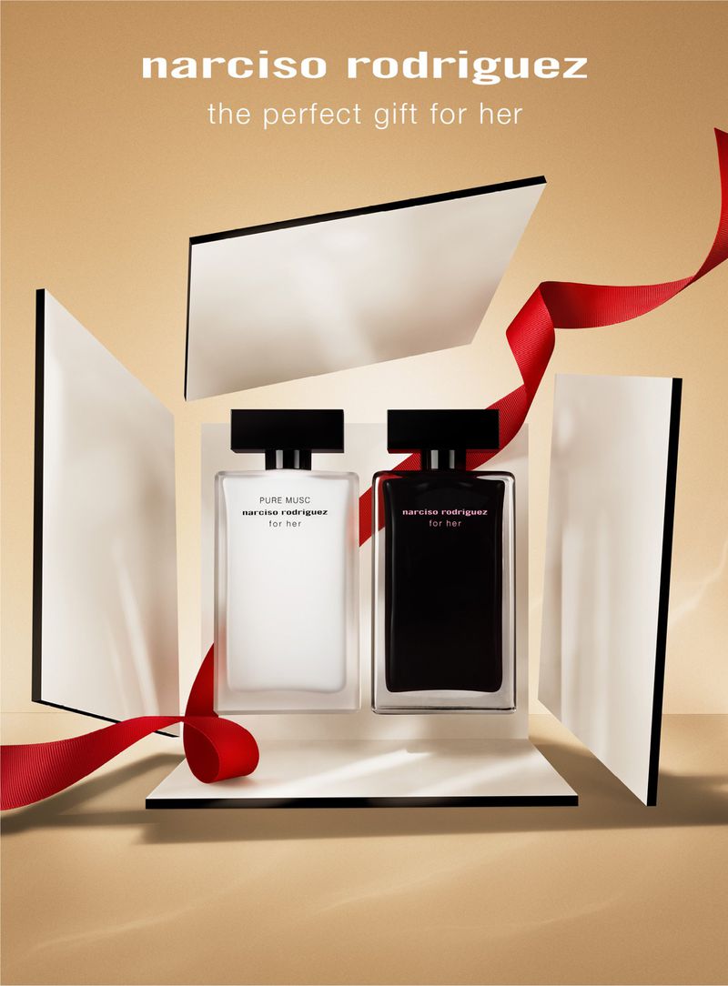 Two Narciso Rodriguez perfume bottles are showcased in an open package, complemented by a red ribbon, set against a tan backdrop.