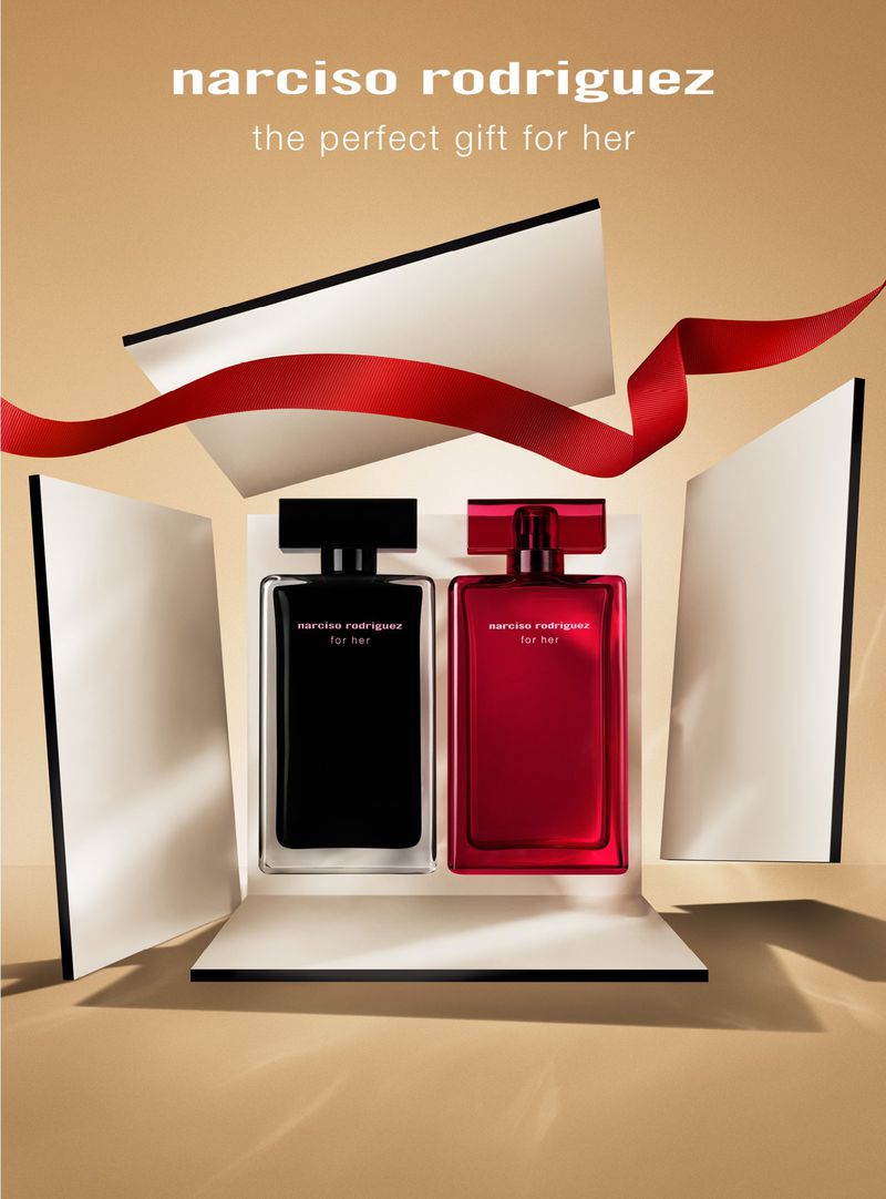 Two Narciso Rodriguez perfume bottles, one black and one red, displayed in a white gift box with a red ribbon on a beige surface.