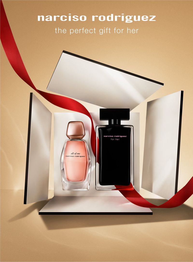 Two Narciso Rodriguez perfume bottles displayed in a white box with a red ribbon against a tan backdrop in a studio shot.
