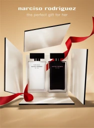 Two perfume bottles displayed inside an opened gift box with a red ribbon against a warm beige background.