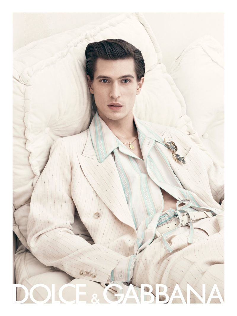 A model poses in Dolce & Gabbana apparel, lying on white cushions in a studio setting, showcasing modern fashion and design.