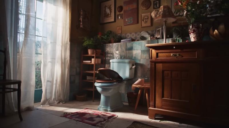 Vintage-style bathroom interior with a light blue toilet, wooden vanity, and natural light streaming through sheer curtains.