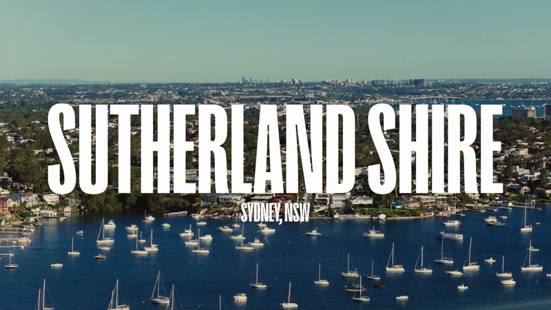 Aerial view of Sutherland Shire, Sydney, NSW, featuring a scenic harbour dotted with sailboats, suburban houses, and distant cityscape.