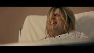Doctor in a hospital room eating a sandwich while a woman in labor lies in a hospital bed with family members around