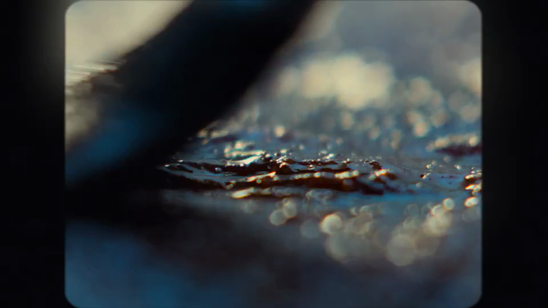 Close-up abstract view of water with light reflections and dark object obstructing the upper portion of the frame on black background.