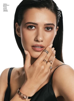 Close-up portrait of a woman with wet-look dark hair wearing multiple rings and a black strap top against white