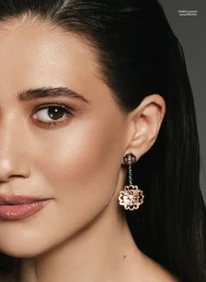 Close-up portrait of a woman with wet-look dark hair wearing a dangling floral pendant earring for an Elle Romania editorial.