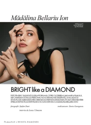 Close-up portrait of Madalina Bellariu Ion wearing a black top and gold jewelry against a grey studio backdrop.