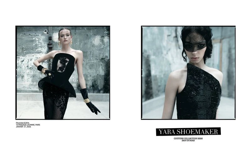 Two fashion models wearing black couture dresses, gloves, and jewelry. One model wears a lace mask. Photographed against a textured gray wall.