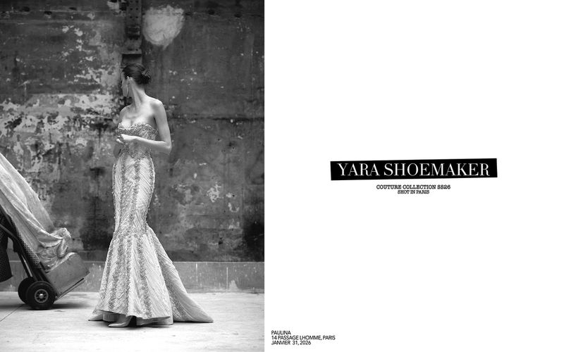 Black and white fashion shot of a woman in a gown, standing near a weathered wall with a trolley, promoting Yara Shoemaker's collection.