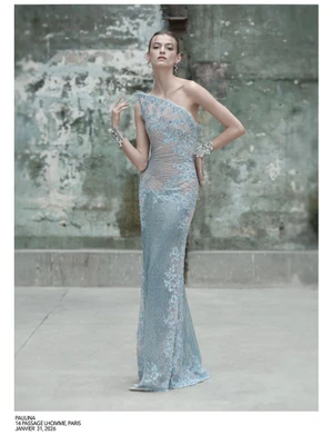 Model Sofia Pilishenko wearing a blue one-shoulder lace gown against a weathered stone wall and concrete floor