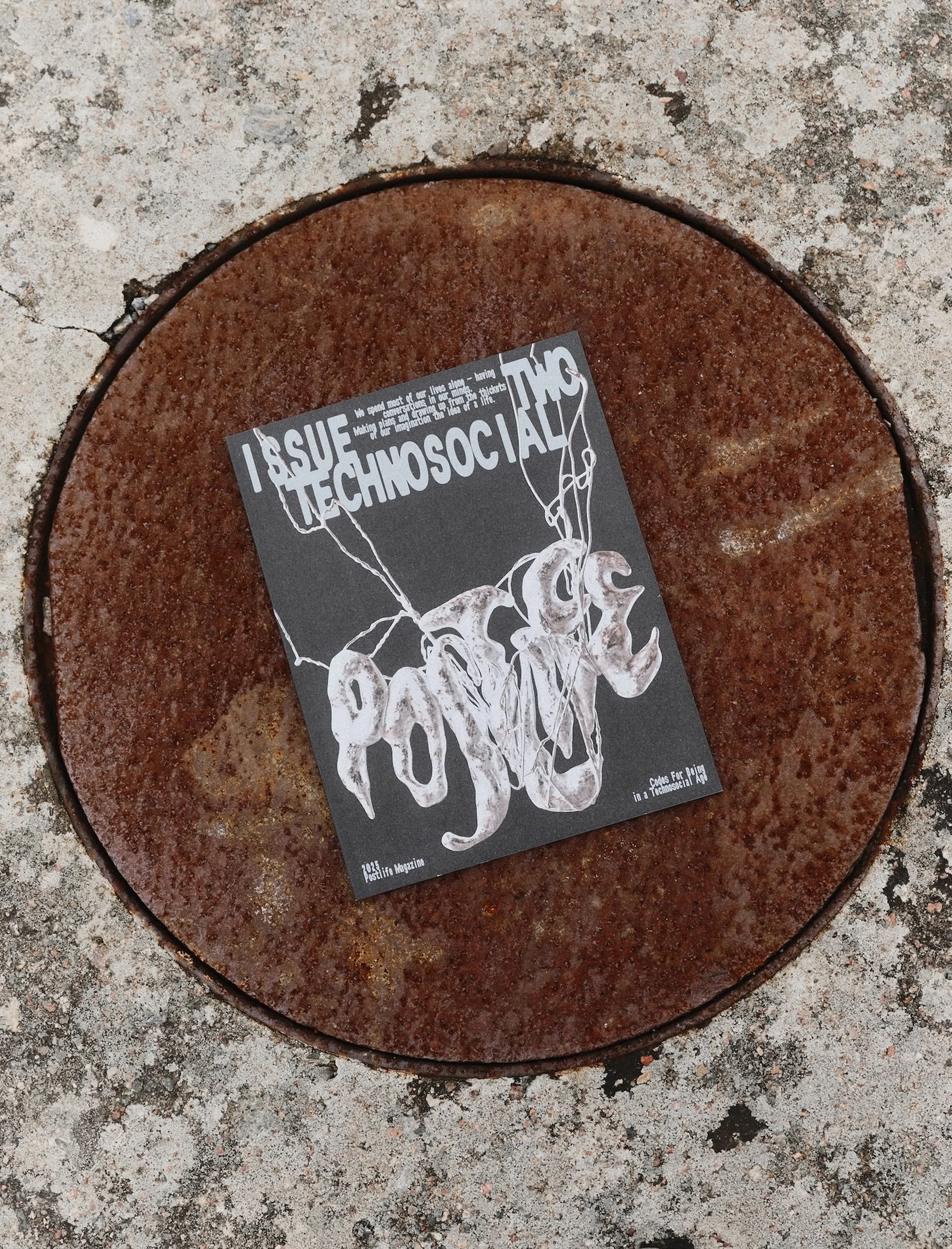 Indie magazine on rusted metal surface features bold typography and abstract line art in contrasting black and white for visual impact.