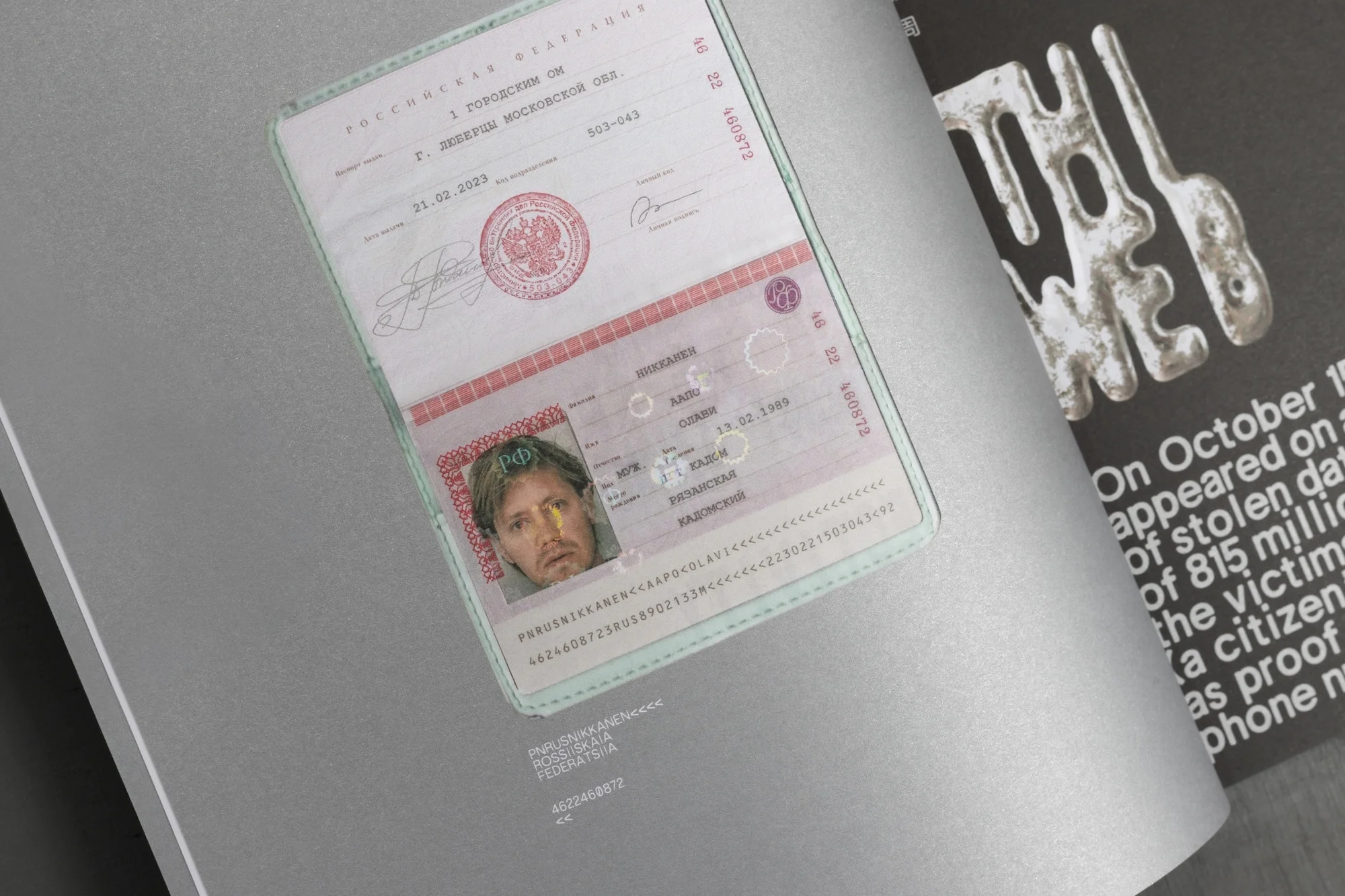 Open Russian passport with photo ID page visible, featuring a man's portrait and official stamps, next to a poster with bold text.