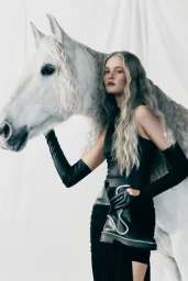 Model wearing black clothing and long gloves holding a white horse against a white backdrop for Rene Caovilla
