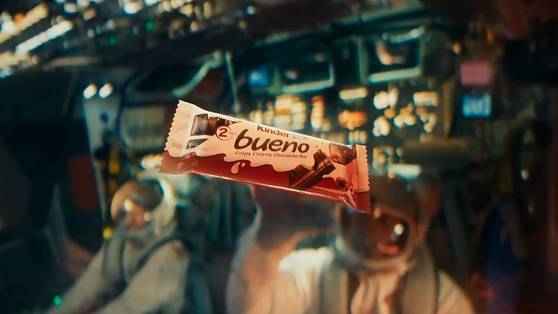 Kinder Bueno chocolate bar floating in a spaceship cockpit with two astronauts, promoting the candy in an unexpected environment.