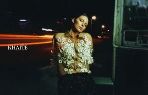 Kendall Jenner in a floral embellished sheer blouse against a nighttime street background with long exposure lights.