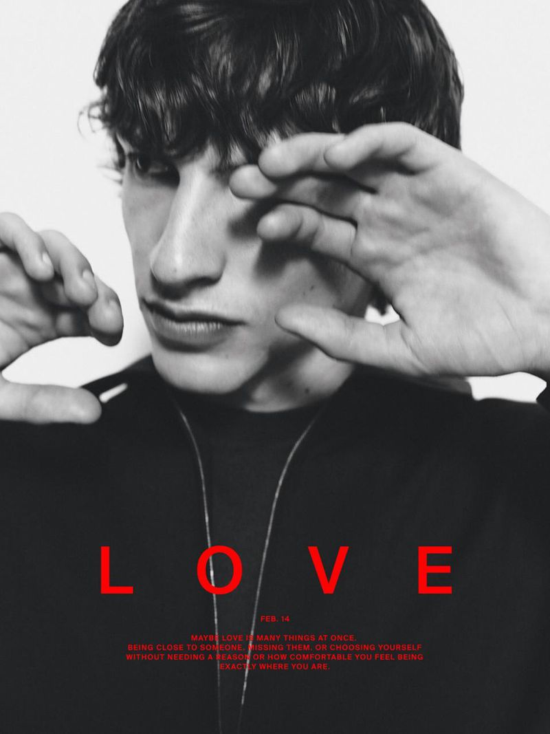 Close-up portrait of a young man with dark hair holding his hand near his face wearing a black top for Massimo Dutti