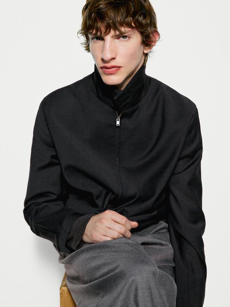 Model wearing a black zip jacket and grey trousers against a white seamless background for Massimo Dutti