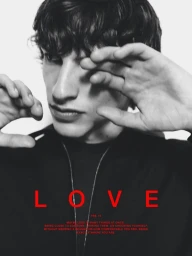 Close-up portrait of a young man with dark hair holding his hand near his face wearing a black top for Massimo Dutti