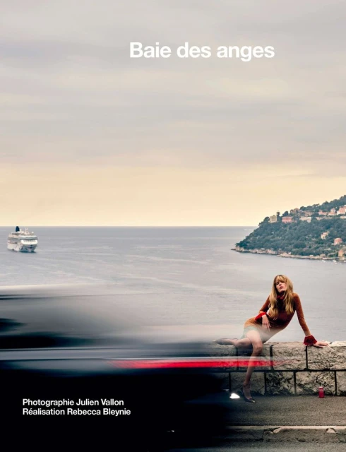 Coastal fashion editorial featuring a long-haired model seated on a stone wall with a cruise ship visible on the ocean.