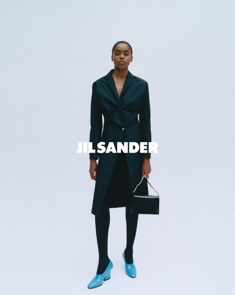 Elegant portrait of a Black female model wearing a black trench coat, black tights, and bright blue high heels against a white background.