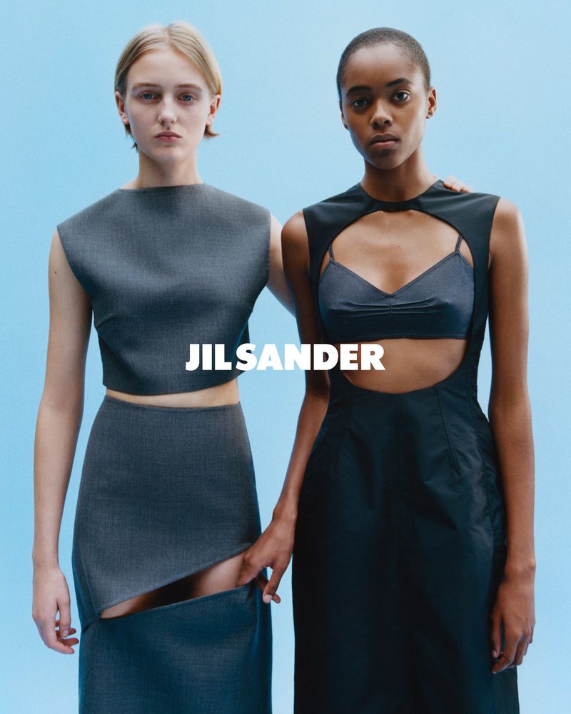 Two women pose in Jil Sander dresses against a bright blue backdrop, showcasing minimalist fashion with a focus on design and style.